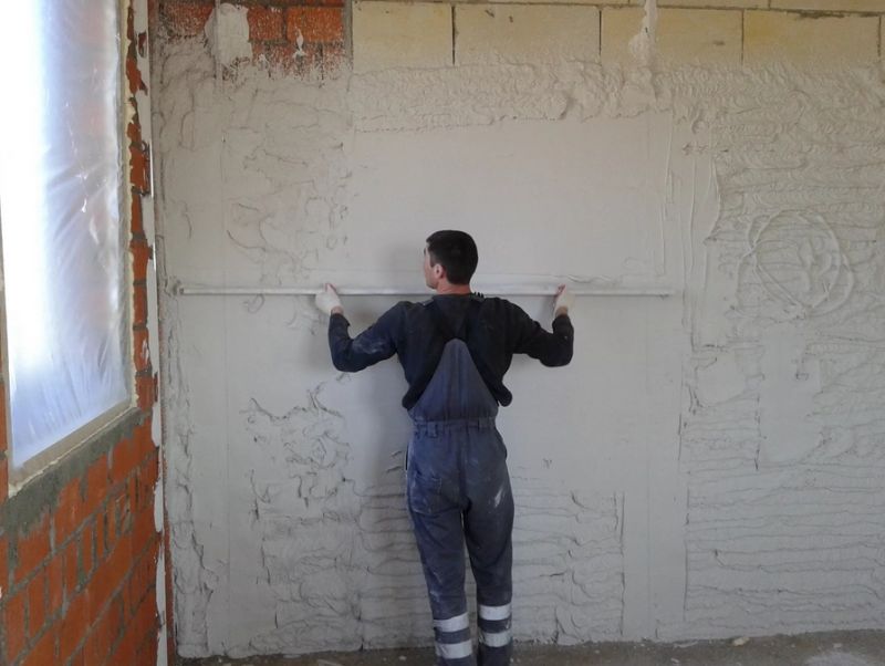 Строитель ровняет стену после штукатурки